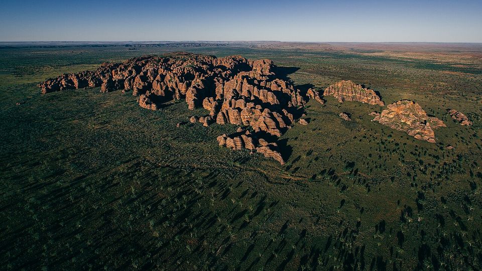 A cluster of orange beehive domes standing alone on a vast green plain in low sun