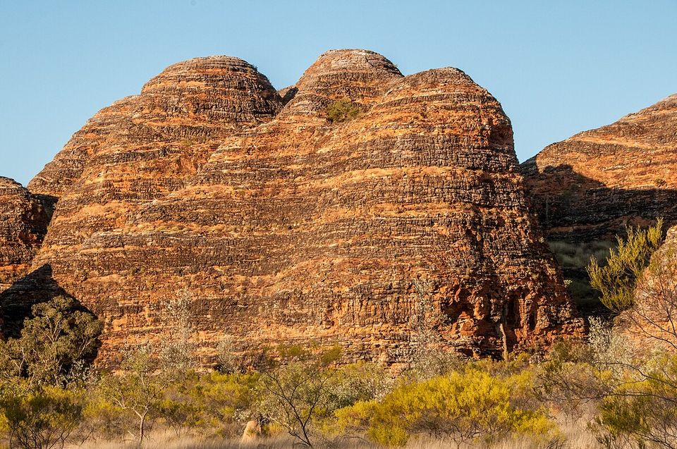 Rounded sandstone domes in horizontal orange and near-black stripes above golden grass in late sun