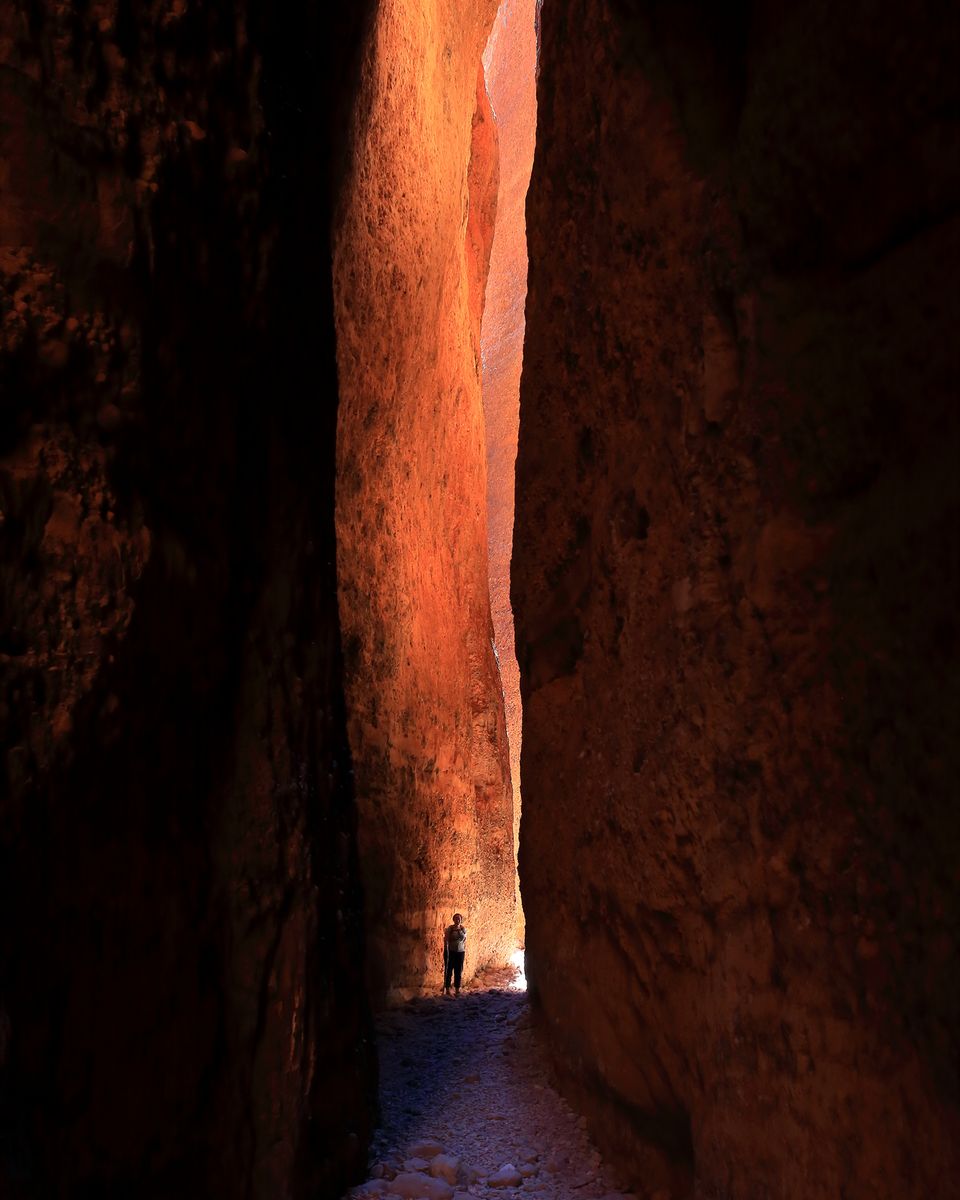 A narrow slot between towering dark walls lit orange high up, a single small walker far below
