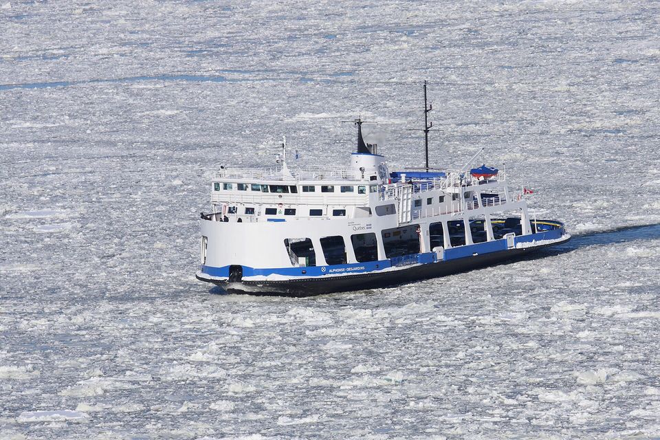 A white and blue ferry pushing through a river covered in broken white ice