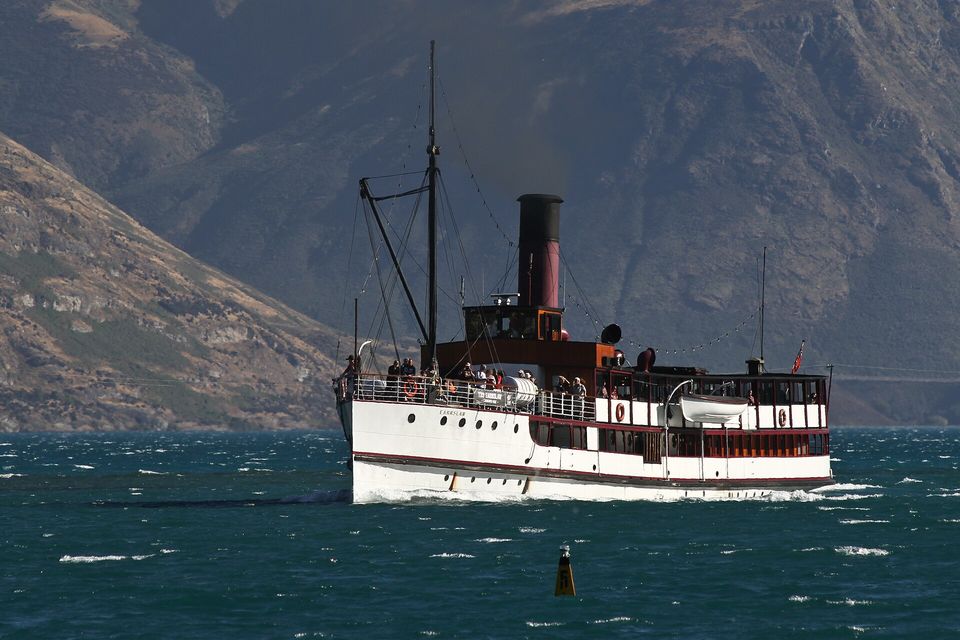 A steamship with a red funnel crossing a lake toward bare brown hills