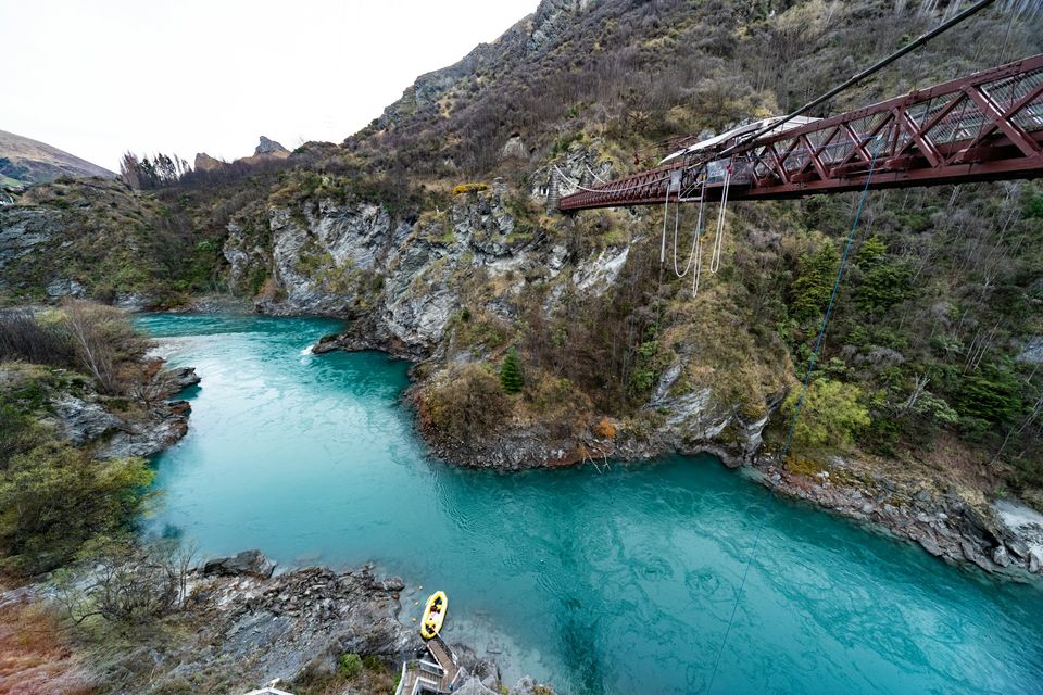 A suspension bridge across a turquoise river gorge with trees on its banks