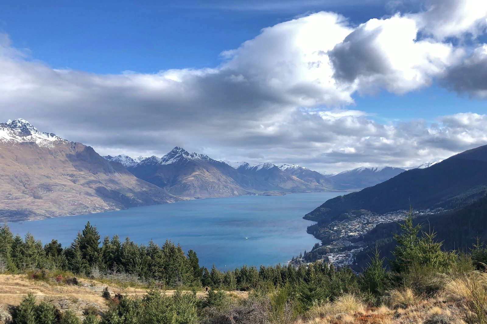 A lakeside town on a bay, a long blue lake running between snow-dusted mountains under broken cloud
