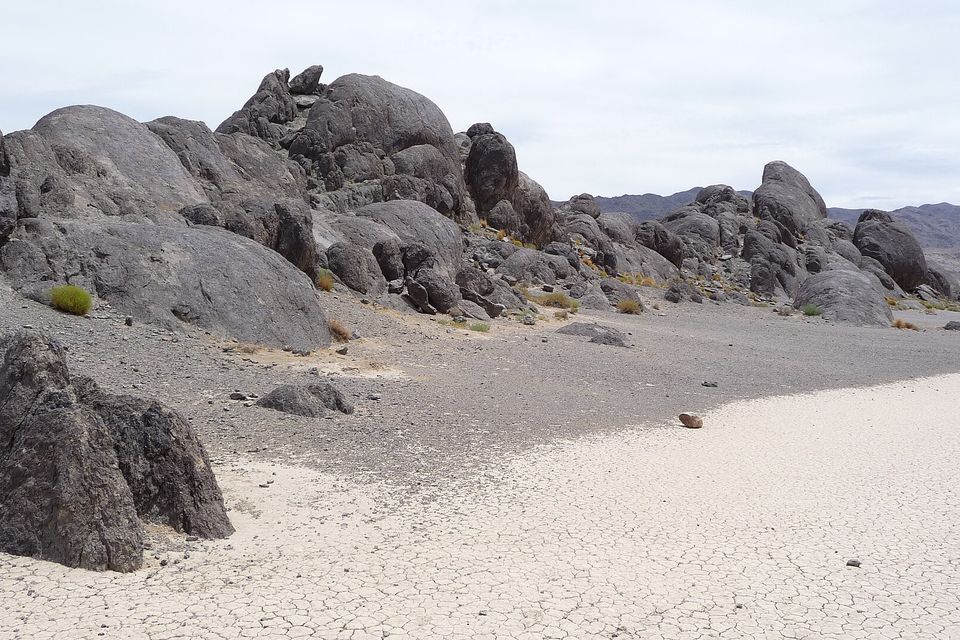 Rounded dark-grey boulders pile up beside a flat white playa of cracked mud, a single small stone sitting on the mud