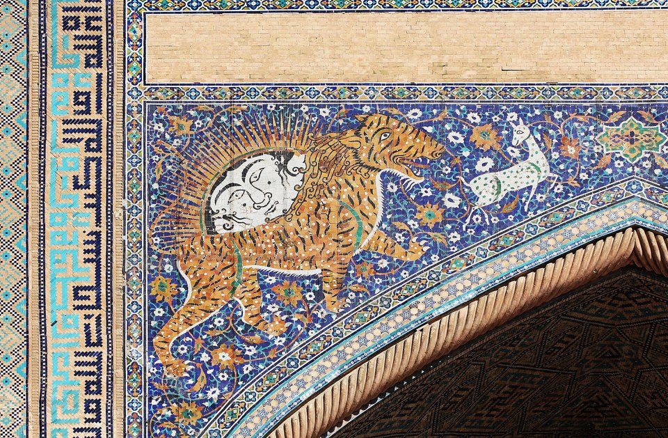 A mosaic of an orange striped tiger chasing a white deer, with a sun with a human face on its back, on a deep blue tiled arch
