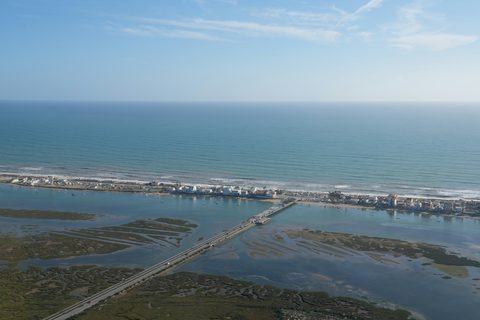 Tidal channels and salt marsh seen from the air, with a bridge to a sandy barrier island and the ocean beyond