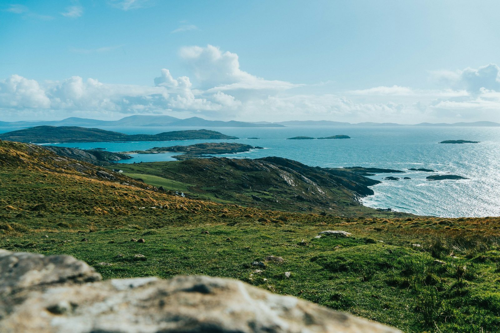 A green headland falling to a bright bay scattered with islands under broken cloud