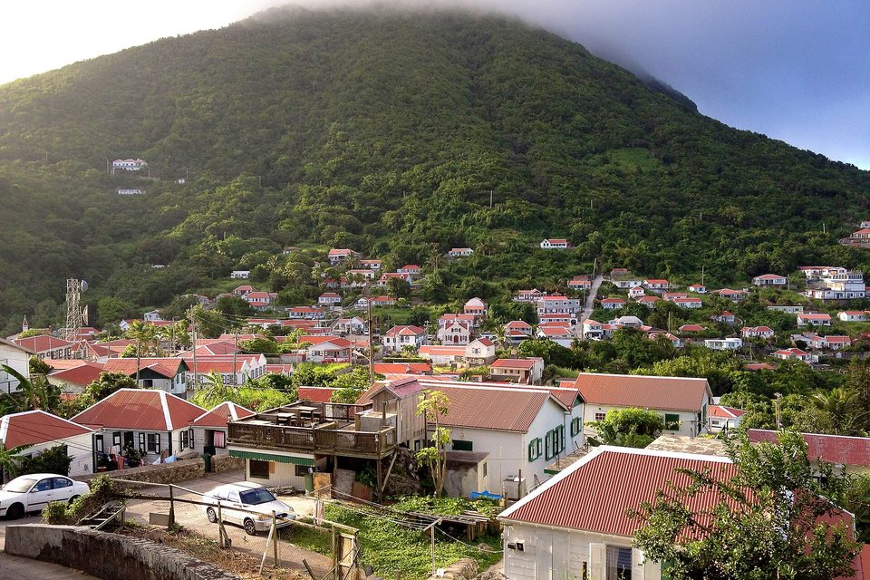 White houses with red roofs on a green slope below a peak capped in cloud