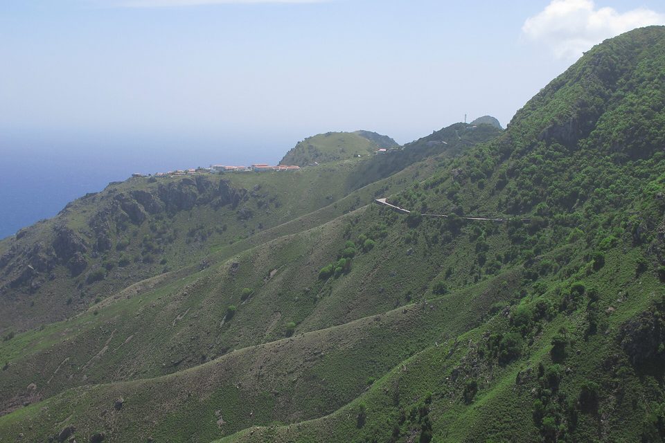 A road cut across steep green slopes high above the sea