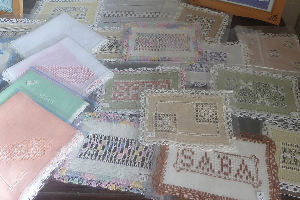 Drawn-thread lace laid out on a table in a museum, one piece spelling out SABA, with handwritten price tags
