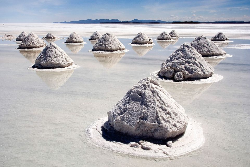 Cone-shaped heaps of white salt in shallow pools on the flat, low mountains on the horizon