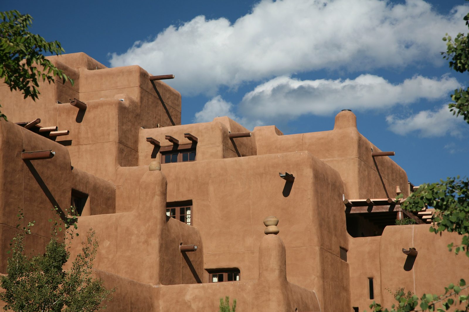 A stepped, rounded adobe building with projecting roof beams under a large blue sky