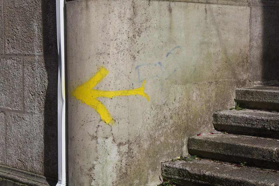 A bright yellow painted arrow pointing left on a weathered grey stone wall, worn granite steps at the right