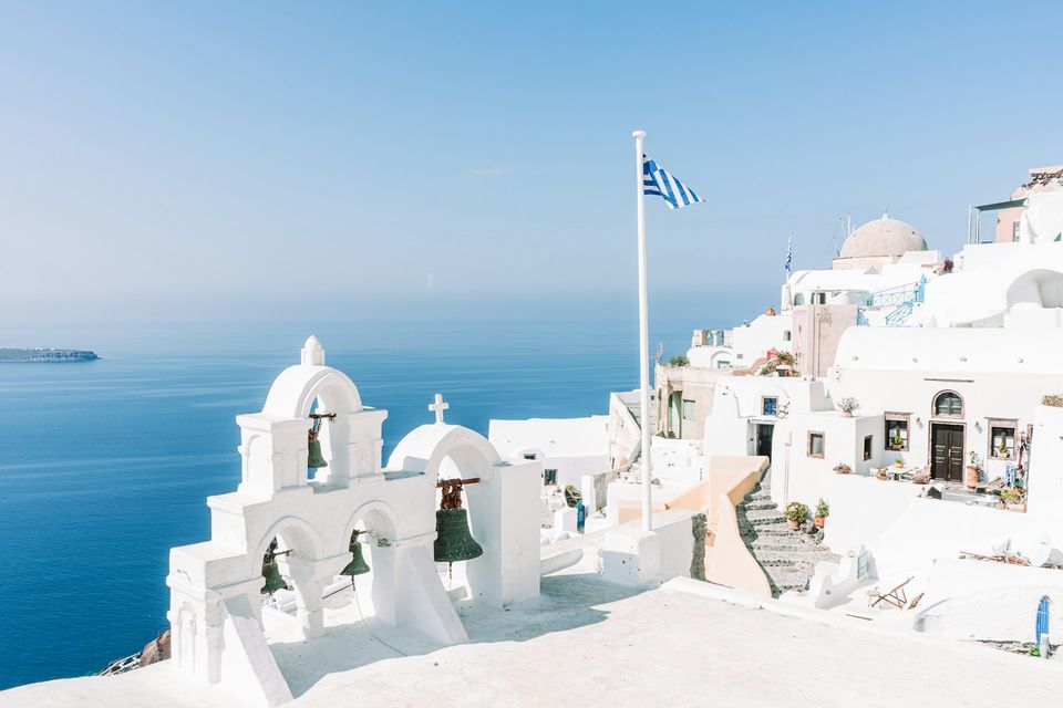 A church bell tower with a flag against a blue sea and a pale sky