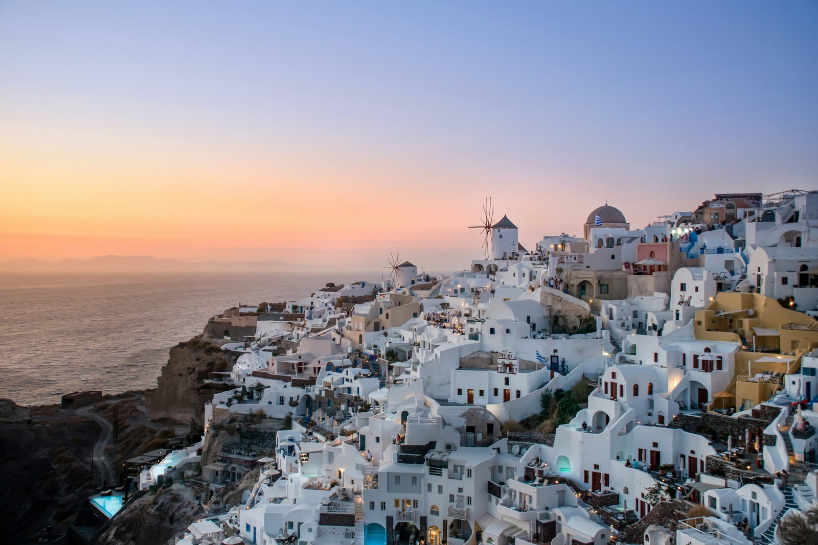 A white village stepping down a cliff beside a windmill, warm afterglow over the caldera