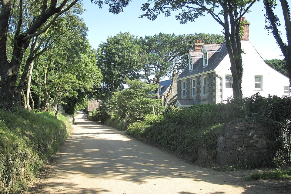 An unpaved lane in dappled tree shade beside stone and white-painted houses
