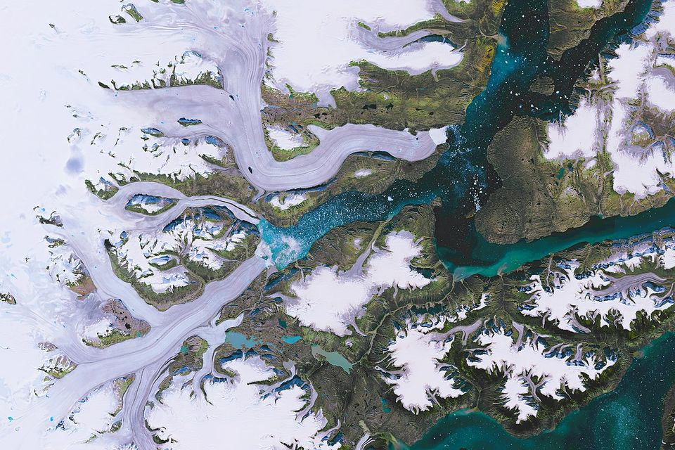 Grey glacier tongues winding between dark mountains into turquoise fjord water dotted with ice