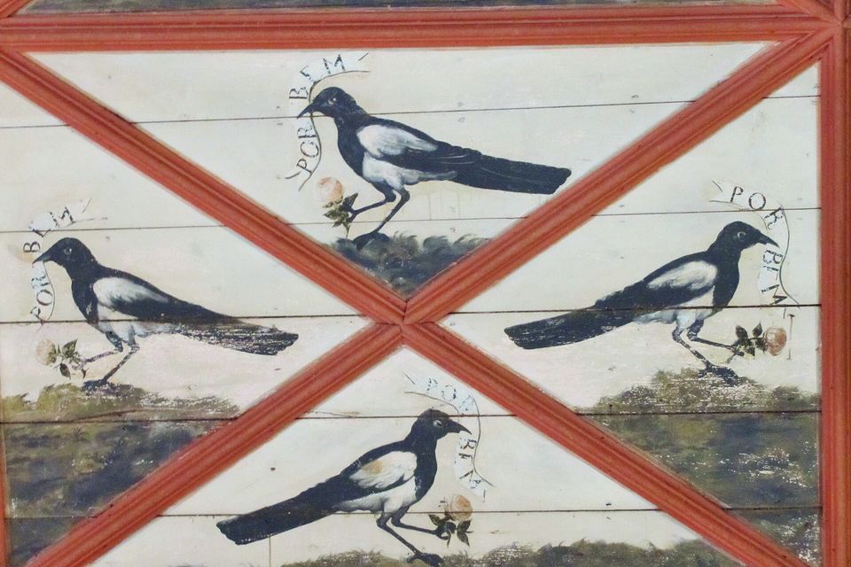 Four painted black-and-white magpies on a panelled ceiling between red diagonal ribs, each holding a rose and a banner reading POR BEM