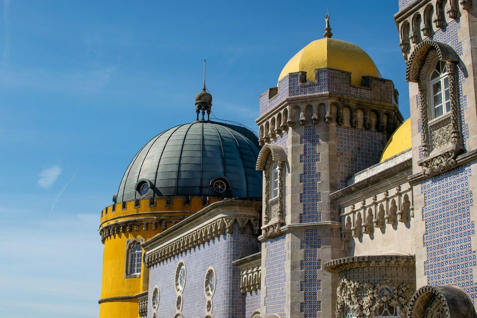 Close view of tiled palace walls, a yellow dome and ornate arched windows under a blue sky