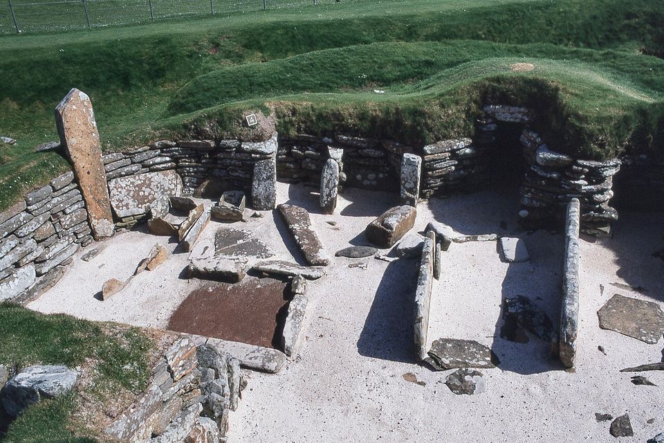 A roofless stone room seen from above, a square hearth in the middle and tall upright slabs along the walls