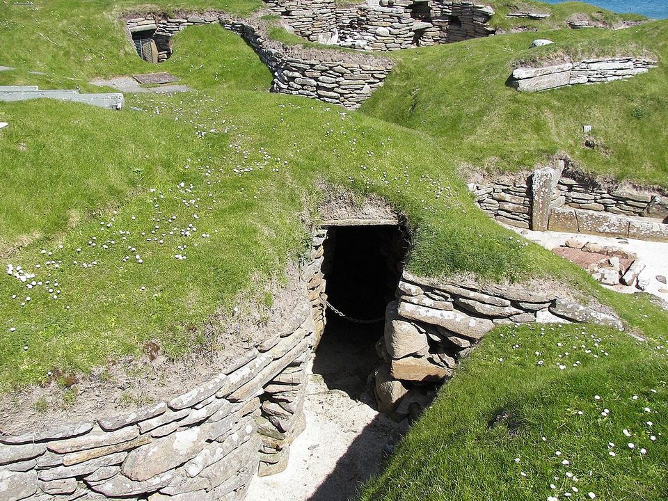 A low stone-lined doorway leading into a dark passage under a grassy mound