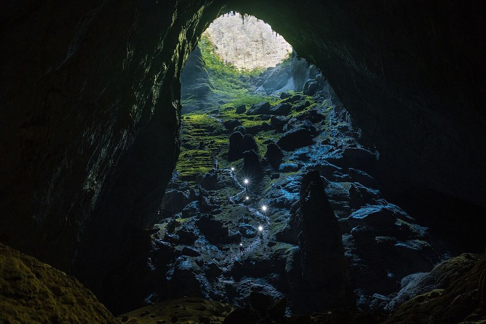 A line of tiny headlamps zigzagging up a boulder slope toward a bright opening far above