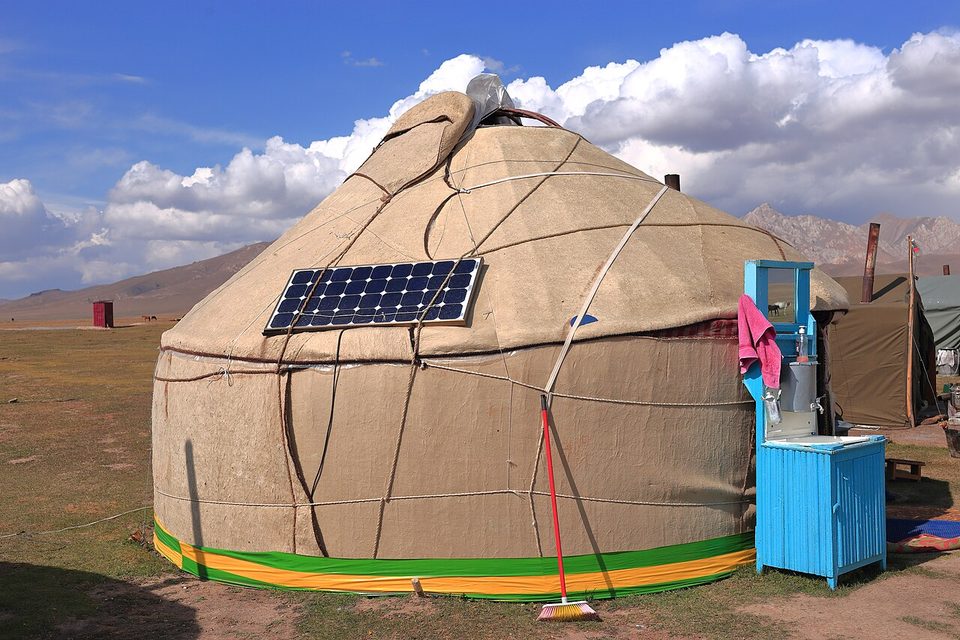 A felt yurt with a solar panel on its roof, and a blue washstand beside it, under a bright cloudy sky