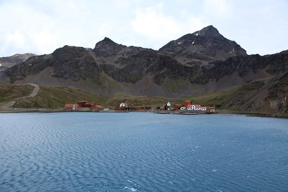 The old whaling station and its church at the foot of steep snowy peaks, seen from the water