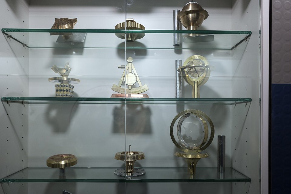 Glass shelves holding brass and steel surveying markers and instruments in a display case
