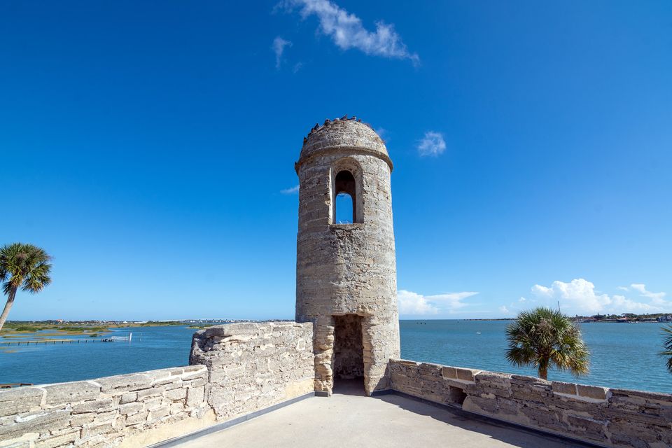 A small stone sentry box on a fort wall with palms and a bay beyond