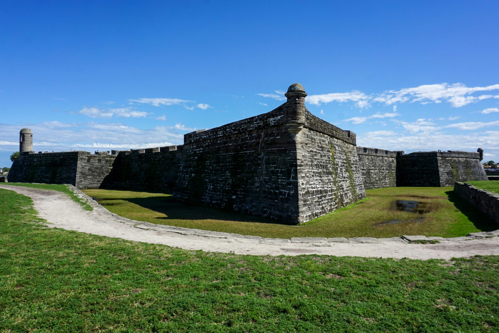 The grey-white walls and a corner bastion of a Spanish fort across a green lawn under a blue sky
