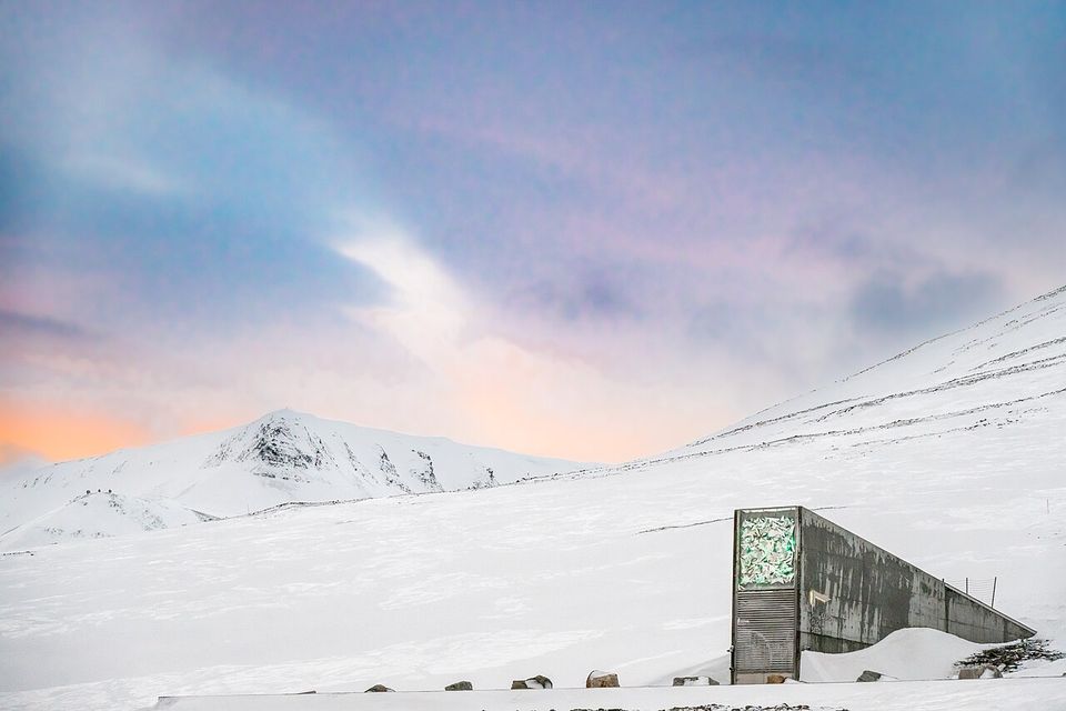 A concrete wedge with a glinting panel jutting from a snowy slope under a pink and blue sky