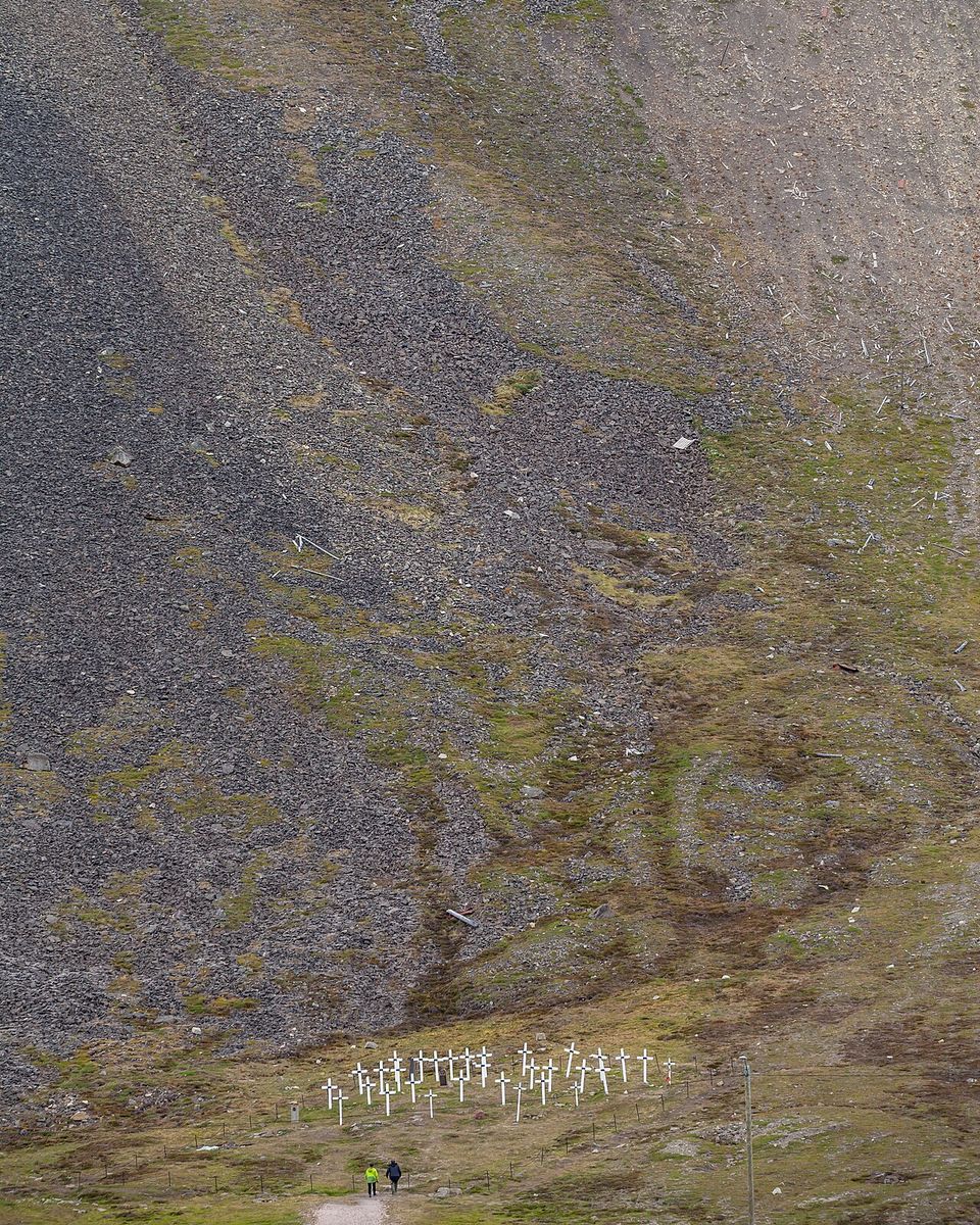 Small white crosses at the foot of a long scree slope, an old timber mine structure high above