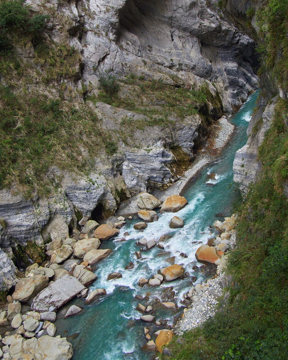 A turquoise river rushing over pale boulders at the foot of grey marble cliffs