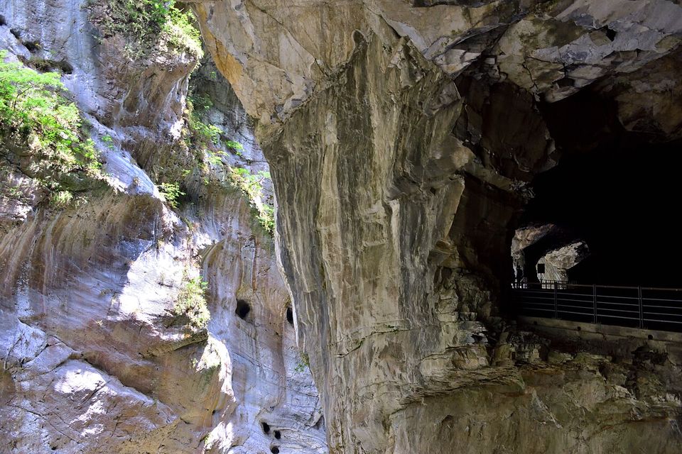A railed walkway tunnelling into a pale marble cliff pocked with small round holes