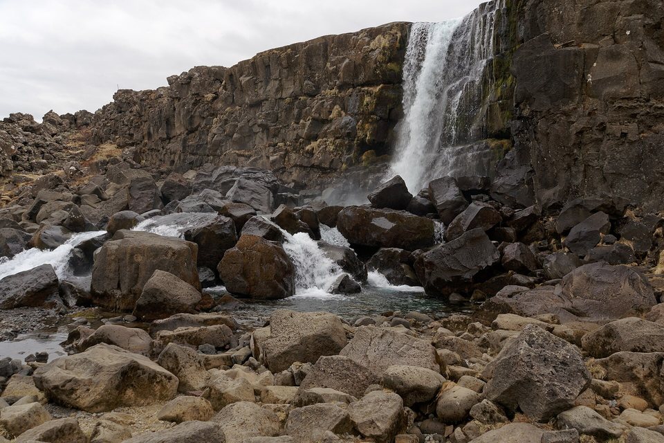 A waterfall dropping over a dark basalt cliff into a boulder-filled stream