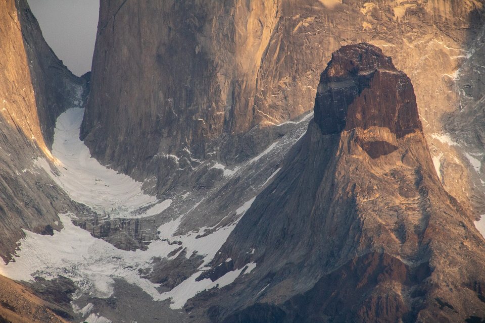 A close view of a pale granite peak topped by a dark brown rock cap, warm dawn light on the cliffs and snow in the gullies