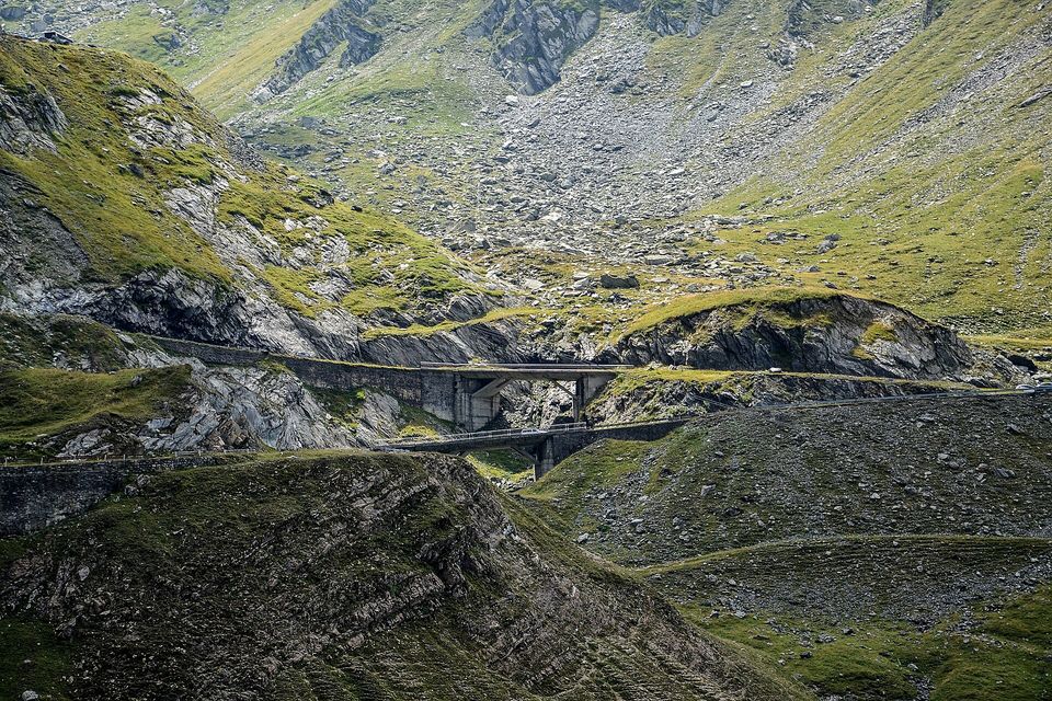 Two stone-faced viaducts stepping across a rocky ravine below pale scree slopes, the road running on beyond them