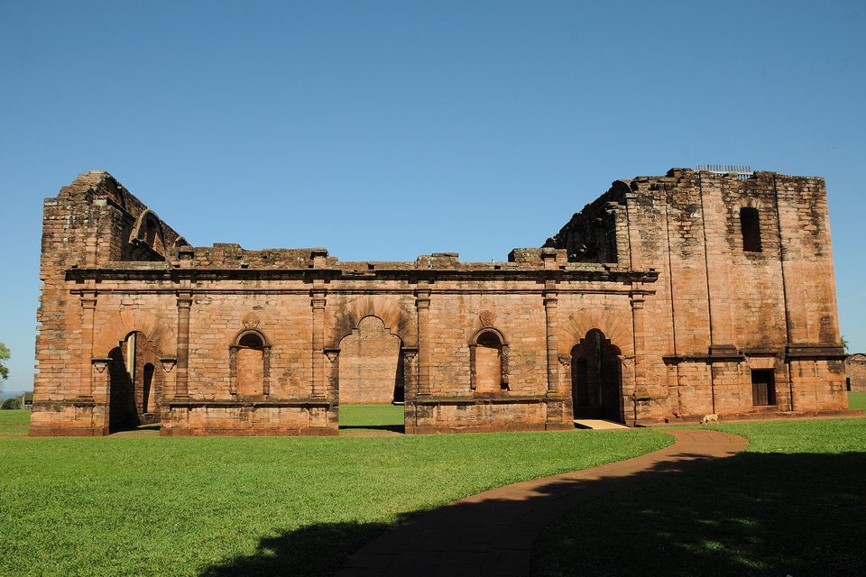 The front of a ruined church with arched doorways under a plain blue sky