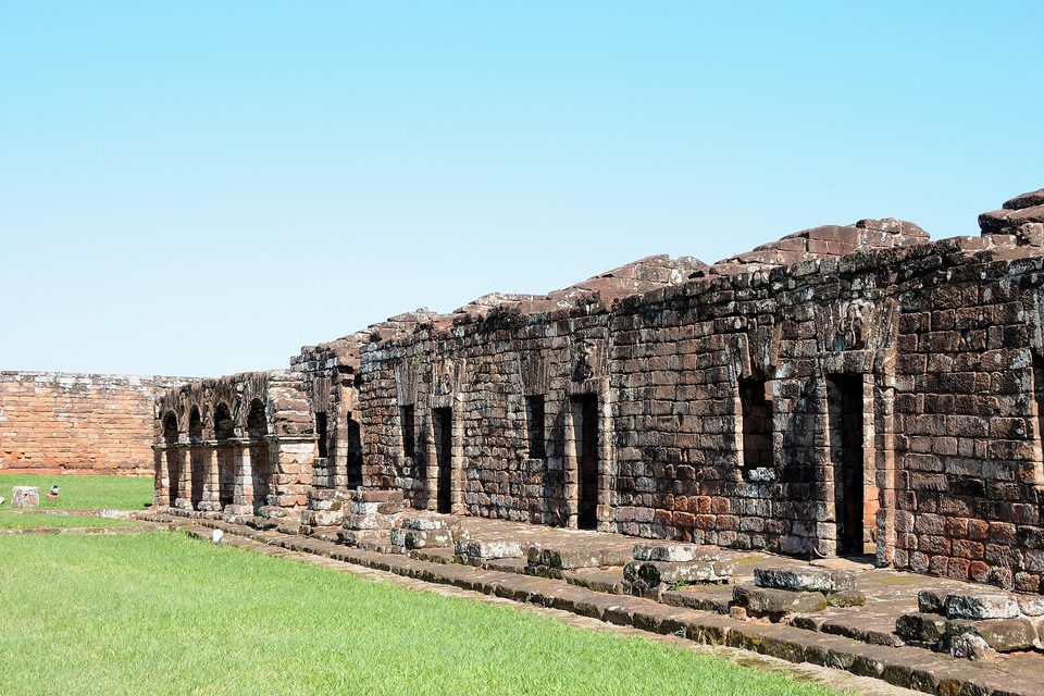 Stone rows of ruined houses with an arcaded walkway on a grassy site