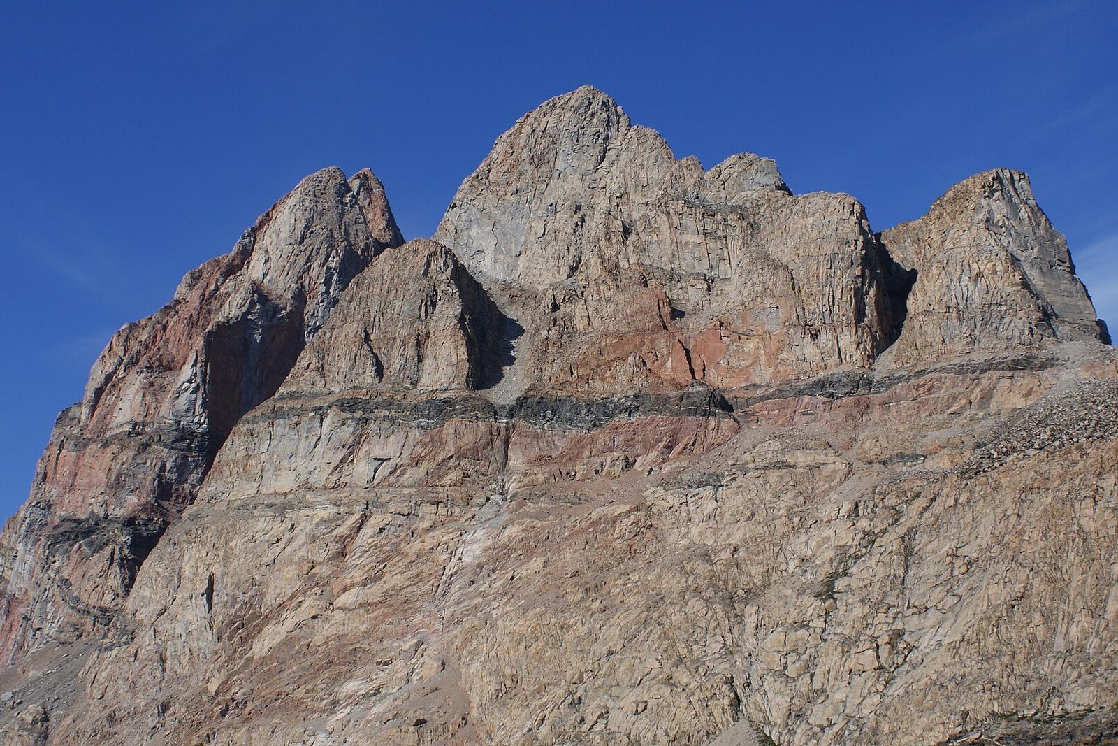A sheer granite mountain with twin summits in side light under a blue sky, a lake in front