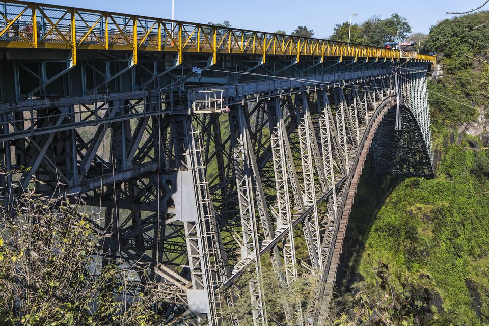 A steel arch bridge with a yellow railing spanning a green gorge