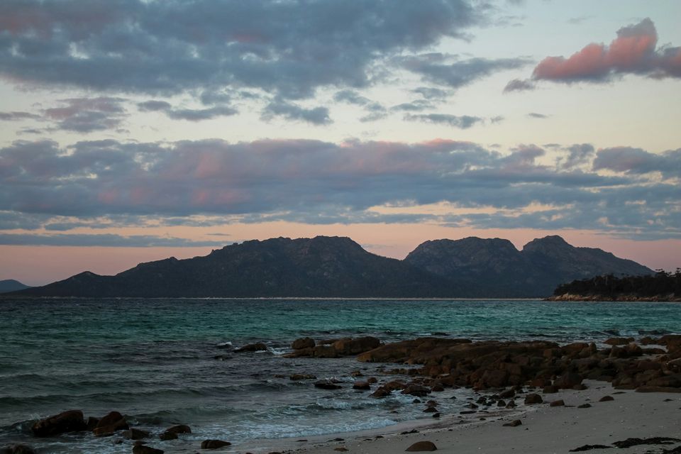 Mountain peaks in silhouette across the water under pink-edged cloud