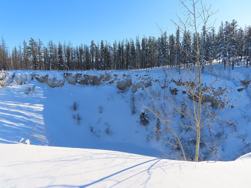 A deep round hollow in snowy forest, its sides ringed with spruce