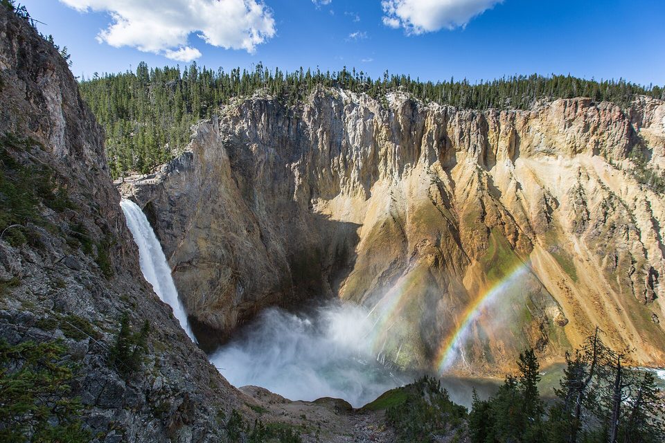 A tall waterfall dropping into a yellow-walled canyon with a rainbow arching through the spray