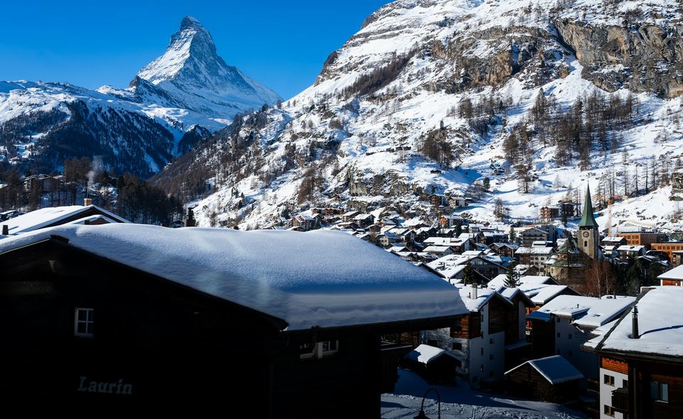 A snowy alpine village, a church spire in the middle and a great peak rising behind