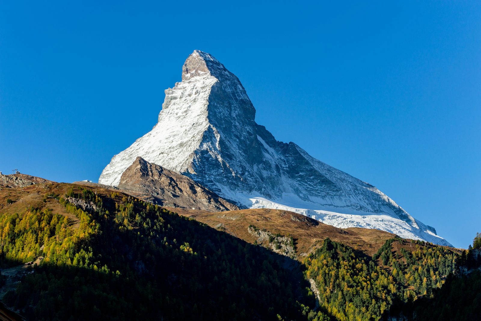 A sharp pyramid mountain with a clear blue sky above and golden larches on the slopes below