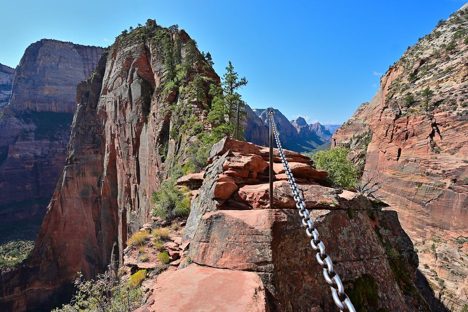 A narrow red sandstone ridge with a steel chain running along it, steep drops to either side and a blue sky above